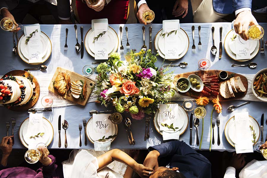 Specialty Lines - Aerial View of a Bride and Groom Kissing While Their Wedding Guests Sit Around a Table Decorated with Flowers and Food